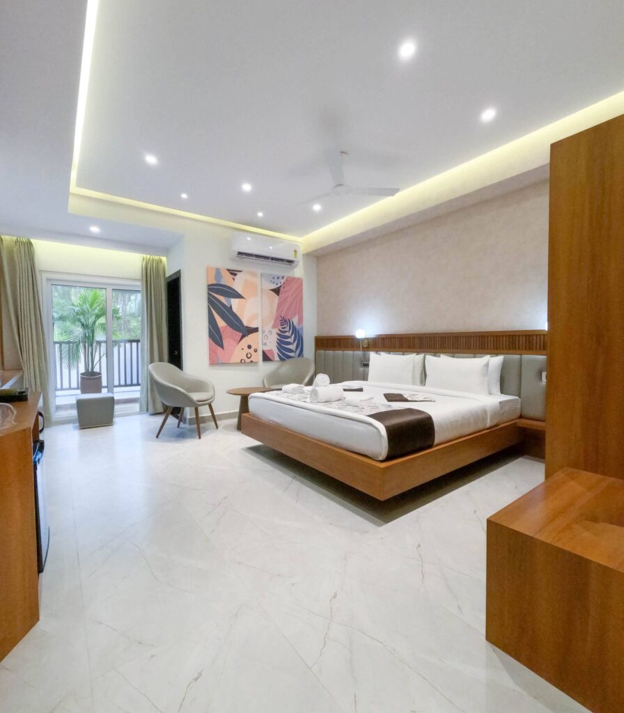 Bright hotel room with a king bed, lounge chairs and a balcony door