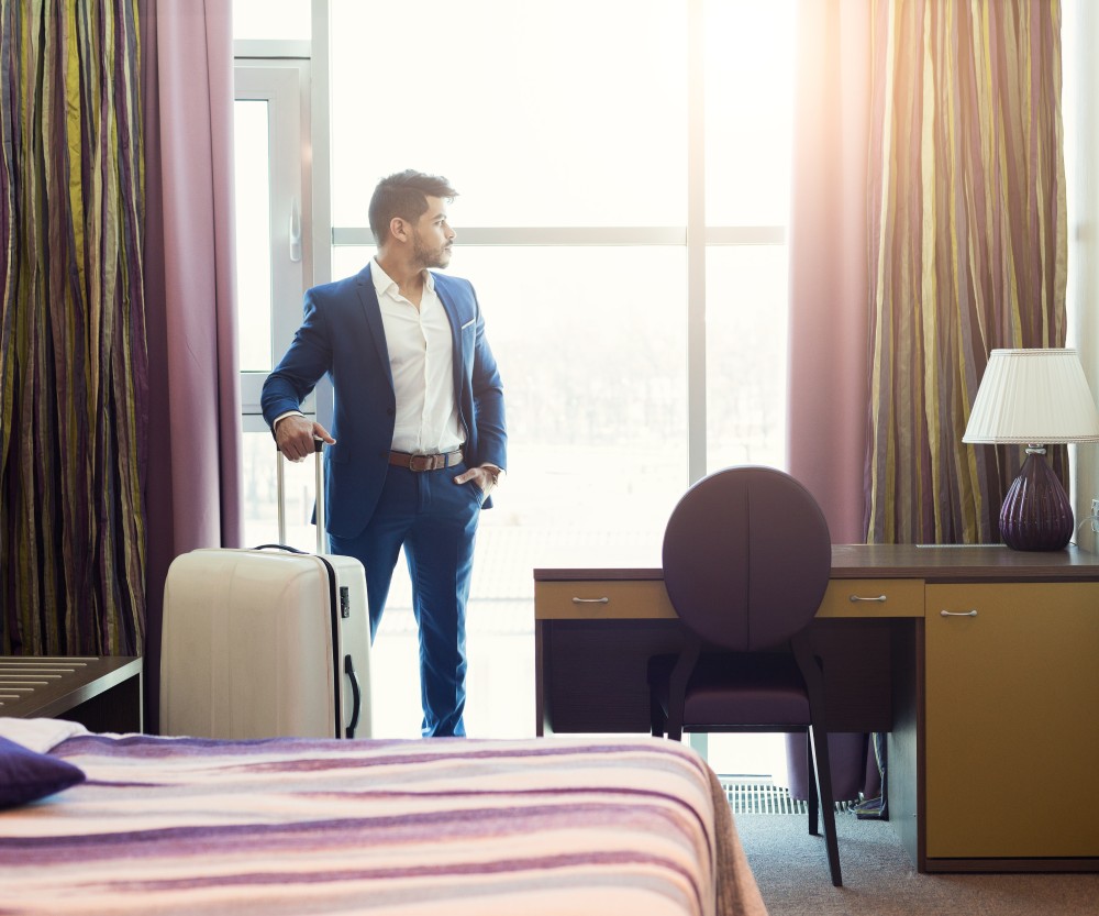 Business traveller with a suitcase looking out of a hotel room window